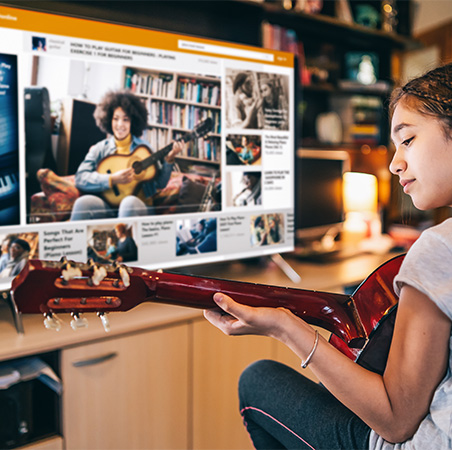 Girl learning how to play guitar from an online video